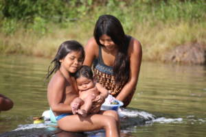 En mor og to barn vasker klær i elva. 
