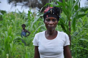 En kvinne med en kurv på hodet står i en åker i DR Kongo. 